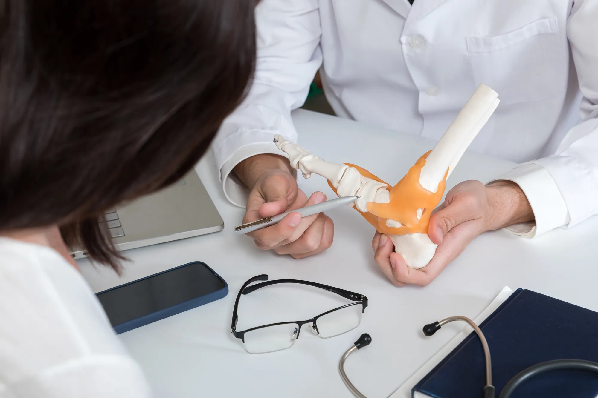 A specialist referring to a model of the human foot in a consultation for chronic instability.